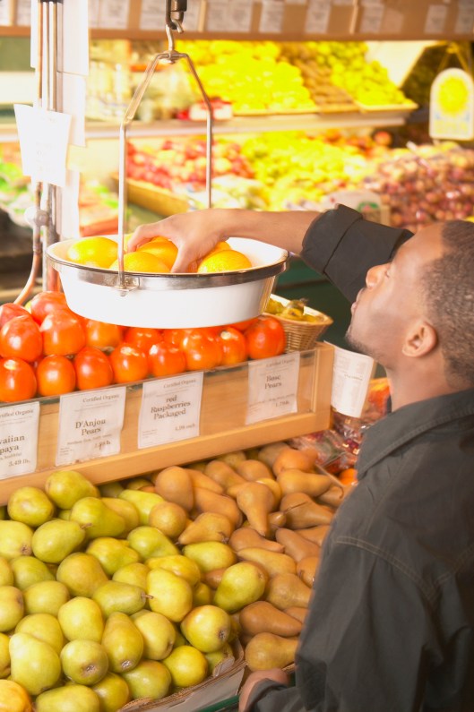 African American man weighing fruit in supermarket scale