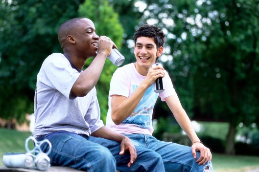 Two Friends Sit Side-by-Side in a Park Drinking Beer