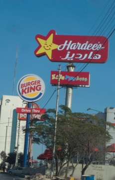 Full-length view of three fast food restaurant signs (Hardees, Burger King, and Popeyes) along a street in Amman, Jordan.